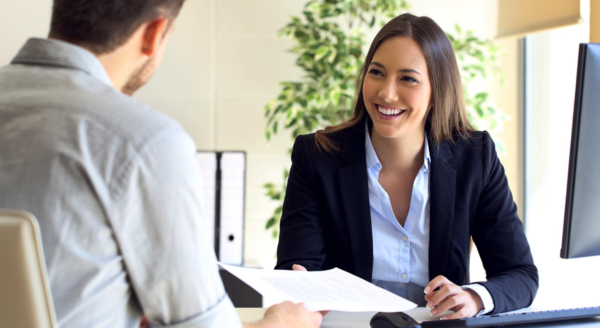 Woman smiling while being handed a document by a man Woman smiling while being handed a document by a man