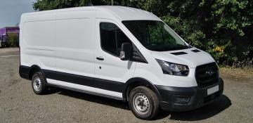 Image shows white long wheelbase van in a gravel carpark, in front of green bushes on a sunny day